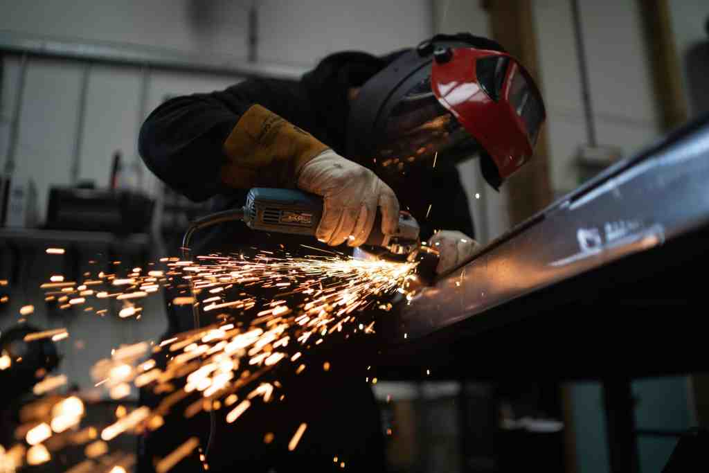 Skilled worker welding metal pipe with sparks flying in industrial workshop.